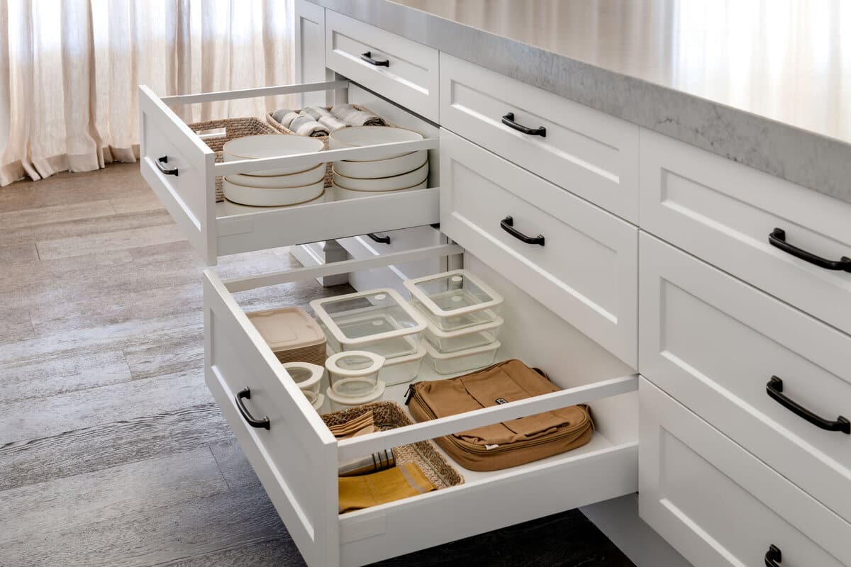 Two open kitchen drawers holding stacked white plates and lidded storage containers.