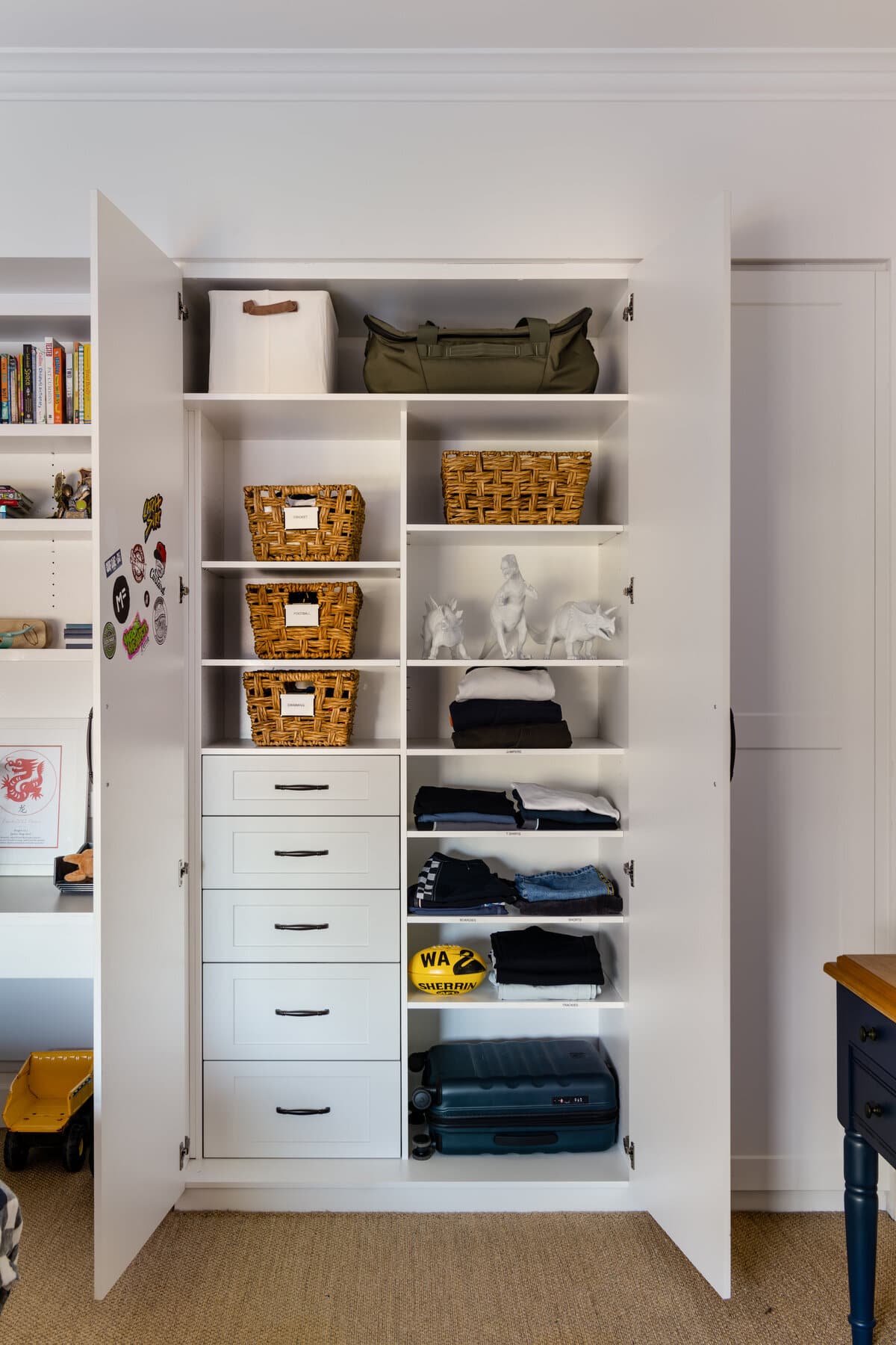 White shelving with woven baskets and a handbag on the upper shelves and folded clothing on the shelves below.
